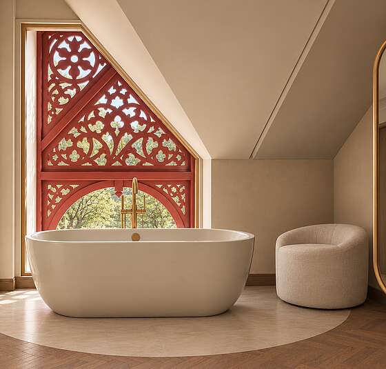 Freistehende Badewanne in der Signature Suite im Art-Déco-Stil vor dem historischen Giebelfenster mit Blick auf den Achensee